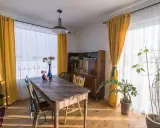 Słoneczne, żółte zasłony tworzą przytulny wystrój okien w stylu retro. Drewniany stół i kredens dodają ciepła.
