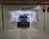 Un coche BMW oscuro espera en un montacoches para garaje. La luz roja del semáforo indica que debe esperar.