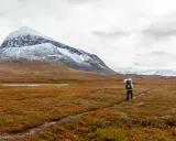 Vandrare på Kungsleden i Sarek med snöklädda berg i bakgrunden och höstens färger i förgrunden.