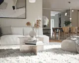 En modern lounge med en vit soffa, ett soffbord i sten och en fluffig matta. I bakgrunden syns en matsal med trästolar, vilket visar olika inredningsstilar.