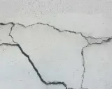 Pęknięcia na jasnej powierzchni betonu, świadczące o procesie karbonatyzacji.