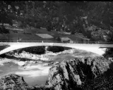 Puente de arco de hormigón de **Robert Maillart** sobre un río rocoso, con colinas boscosas al fondo.