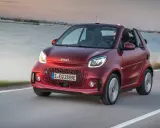 El Smart EQ Fortwo, cual es el coche más pequeño del mercado, se desplaza ágilmente por una carretera costera al atardecer.