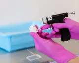 Ręce w różowych rękawiczkach trzymają pistolet do przekłuwania uszu i kolczyk. To instrukcja, jak zdjąć kolczyki pierwsze.
