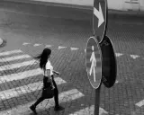 Donna attraversa la strada, un momento catturato con la street photography tecnica. Segnali stradali indicano la direzione.