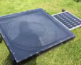 Un système de chauffage air solaire avec un panneau de tubes noirs en spirale sous une couverture transparente, à côté d'un petit panneau solaire.