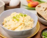 Cremiger Eiersalat mit Joghurt und Gurke, garniert mit Frühlingszwiebeln, serviert mit Brot.