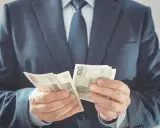 Mężczyzna w garniturze liczy banknoty 100 zł. To jego zabezpieczenie finansowe na przyszłość.