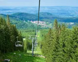 Wjazd kolejką na wysoką kopę trasę, otoczoną lasem świerkowym. W oddali widać zabudowania i góry.