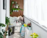 Przytulna loggia w bloku z wygodną kanapą, ziołami na półkach i bukietem kwiatów. Idealne miejsce na relaks.
