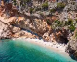 Versteckter geheimtipp kroatien strand: Eine kleine Bucht mit türkisfarbenem Wasser, umgeben von steilen Felsen. Einige Boote liegen am Ufer, wenige Menschen genießen die Ruhe.