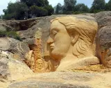 En la ruta de las esculturas, rostros emergen de la roca. Una gran cabeza femenina domina la escena, flanqueada por figuras más pequeñas.