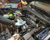 Mechanik w niebieskich rękawiczkach trzyma nowe świece żarowe, przygotowując się do ich wymiany w silniku samochodu.