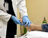 Un professionnel de santé examine un pied, possiblement pour une plaie diabétique, avec des gants bleus. L'application de bétadine est une étape courante pour le soin des plaies.