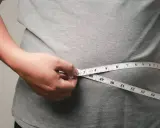 Eine Hand misst mit einem Maßband die Taille. Viele fragen sich, wo nimmt man zuerst ab – oft ist es der Bauch.