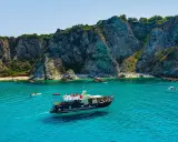 Barca turistica naviga nelle acque cristalline vicino al porto di Tropea, con imponenti scogliere a picco sul mare e piccole spiagge affollate.