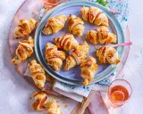 Petits croissants au jambon dorés, certains saupoudrés de graines de sésame ou de pavot, prêts à être dégustés.