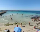 Gente in spiaggia e in mare vicino alla torre vado lungomare. Acqua cristallina e cielo azzurro.