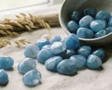 Tumbled quarzo blu, con il suo significato di calma e chiarezza, sparge serenità su un tessuto grezzo, accanto a spighe di grano e conchiglie.