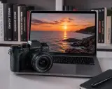 Fujifilm X-T3 accanto a un laptop con tramonto sul mare. Libri di fotografia sullo sfondo.