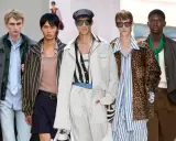Five models showcase bold gay men fashion on a runway, featuring a mix of stripes, leopard print, and stylish outerwear.