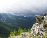 Skalisty szczyt w Zakopanem z widokiem na gęsto zalesione doliny Tatr pod burzowym niebem.