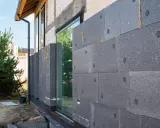 Graue Dämmplatten werden an der Hauswand angebracht, um das Haus zu isolieren.