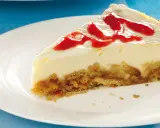 Ein Stück cremiger cheesecake mit keksboden, garniert mit rotem Fruchtpüree auf einem weißen Teller.