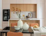 Dos jarrones blancos con flores anaranjadas y amarillas, cuencos apilados y un bol con panecillos son elementos decorativos que poner encima de una mesa de comedor.