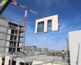 Grúa elevando un módulo prefabricado para la construcción industrializada de un edificio. Obreros supervisan la operación.