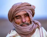 Porträt eines alten Berber Hirtennomaden mit einem Turban und traditioneller Kleidung, dessen Gesicht von der Sonne gezeichnet ist.