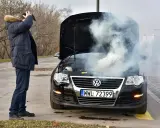 Mężczyzna zrezygnowany patrzy na dymiący, lekko przytarty silnik czarnego Volkswagena.