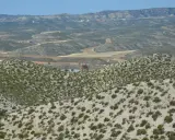 Paisaje árido del desierto de Monegros con colinas cubiertas de matorral y una torre de iglesia solitaria al fondo.
