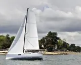 Voilier blanc moderne naviguant sur l'eau, avec des avis sur le Pogo 30. Paysage côtier verdoyant en arrière-plan.