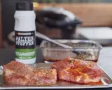 Zwei Steaks liegen auf einem Blech, bereit für die beste Steak Marinade. Daneben eine Flasche "#ALTER PFEPPER" Grillmarinade.