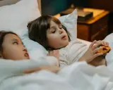 Dos niños en la cama, uno con un coche de juguete, quizás planeando travesuras o contando mentiras en niños de 10 a 12 años.
