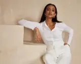 Mujer con maquillaje fiesta ibicenca, luce un conjunto blanco y pendientes dorados, apoyada en escalones de obra.