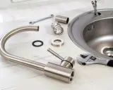 Partes de un fregadero y herramientas listas para su instalación. Llave inglesa, grifo desmontado y el propio fregadero de acero inoxidable.