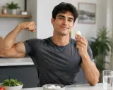 Muskulöser Mann zeigt Bizeps und hält ein gekochtes Ei. Er setzt auf proteinreiche Ernährung mit Ei für seine Fitness.