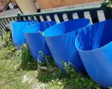 Cuatro grandes barriles azules listos para recoger agua de lluvia en el campo.