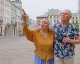 Starsze małżeństwo odkrywa urokliwe, przyjazne seniorom miasta. Kobieta z aparatem wskazuje na zabytkową architekturę.