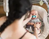 Maluszek w bujaczku polecanym przez fizjoterapeutów. Mama delikatnie głaszcze go po główce, uspokajając.