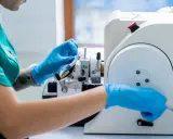 Laborantka w niebieskich rękawiczkach pracuje przy mikrotomie. Czy biopsja jest bezpieczna? Tak, dzięki precyzyjnym narzędziom i doświadczeniu.