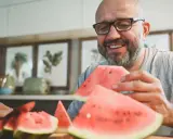 Glücklicher Mann mit Brille isst Wassermelone. Die Wassermelone Nachteile sind, dass sie schnell aufgebraucht ist.