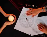 Dwie dłonie nad kartą z horoskopem i świecą. Jedna dłoń trzyma płonącą świecę, druga wskazuje na wykres, analizując swój 6 rok numerologiczny.