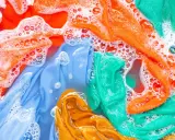 Ropa de color lavadora con burbujas de jabón. Prendas naranjas, azules, verdes y amarillas sumergidas en agua.