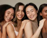 Quatre femmes souriantes aux teints variés, partageant un moment de complicité. Leur peau rayonne, signe qu'elles savent comment hydrater sa peau en profondeur.