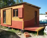 Maisonnette en bois aux couleurs vives, rappelant un nuancier peinture suédois. Porte coulissante jaune, volets rouges.