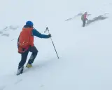Dwóch alpinistów wspinających się po ośnieżonym zboczu. Jeden z nich ma na nogach raki, a drugi używa czekana.