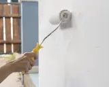 Mano aplicando imprimación a paredes con rodillo. Preparando la superficie para pintar.